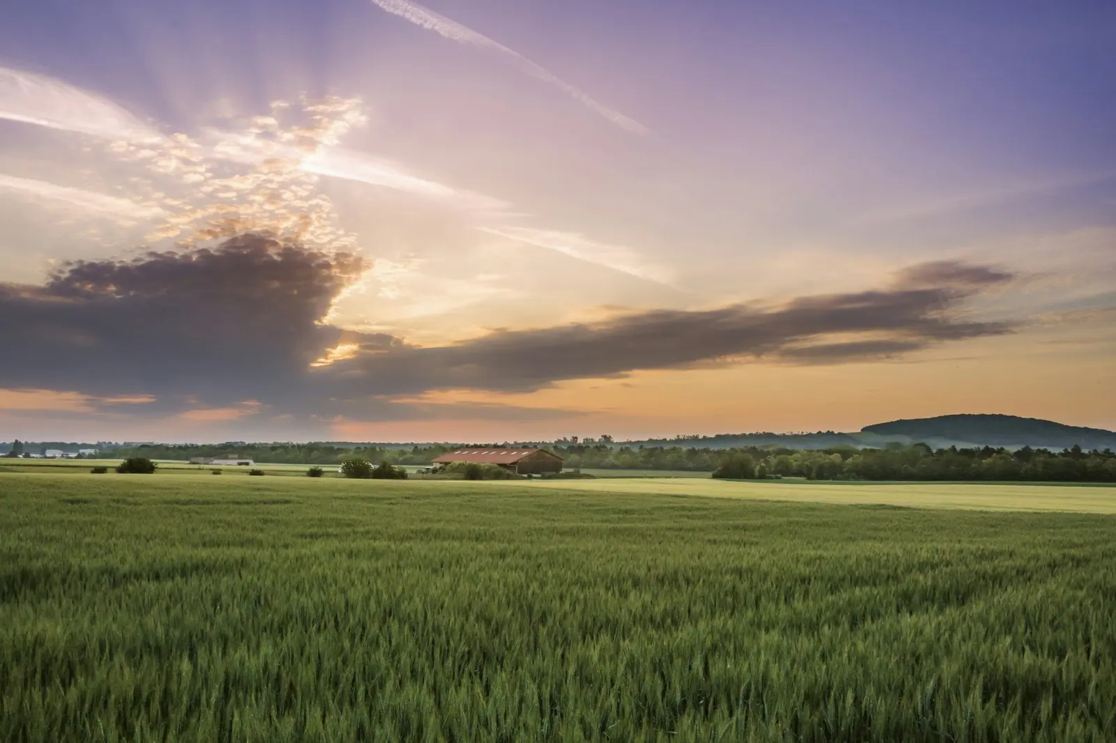 Weite Felder mit einem Bauernhof unter dem Abendhimmel